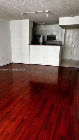 an view with an empty room with wooden floor and a kitchen