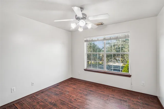 an empty room with wooden floor chandelier fan and windows