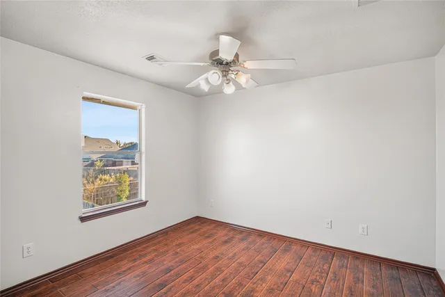 an empty room with wooden floor chandelier fan and windows