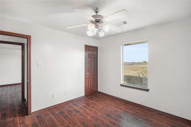 an empty room with wooden floor chandelier fan and windows