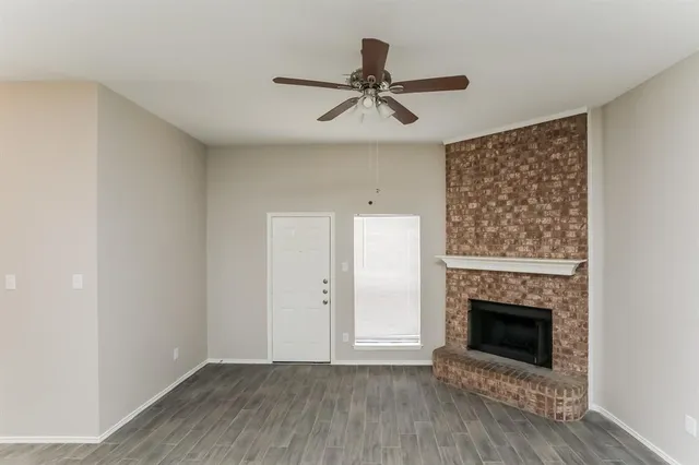 a view of an empty room with wooden floor a fireplace and a window