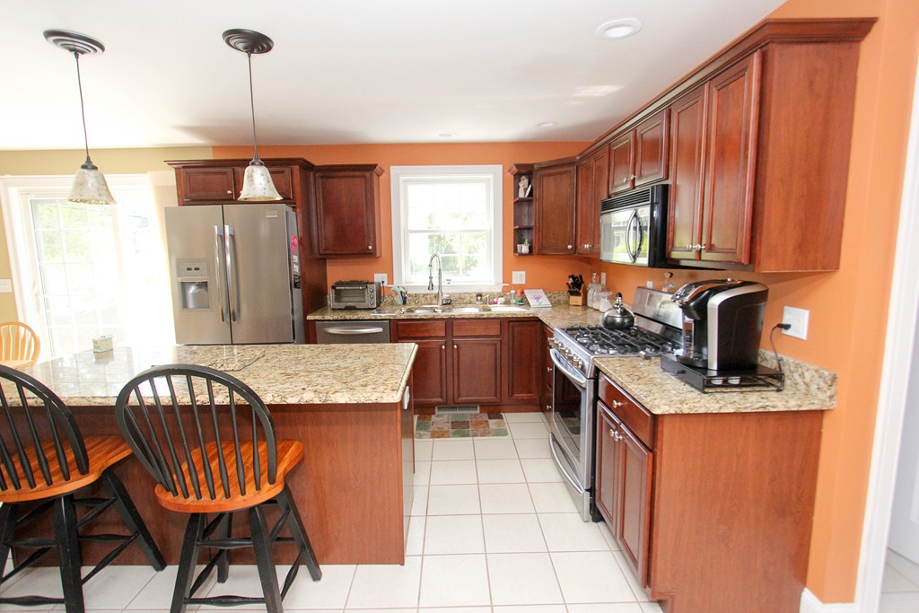7 Middle Road Amesbury, MA 01913 - Photo 3 of 25 a kitchen with stainless steel appliances granite countertop wooden cabinets a sink dishwasher a dining table and chairs with wooden floor