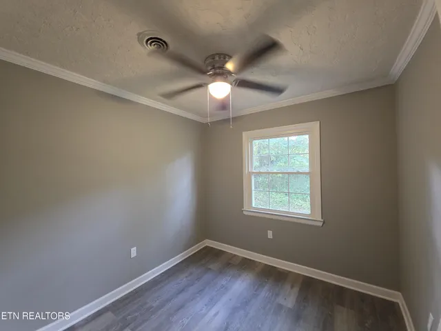 an empty room with wooden floor ceiling fan and windows