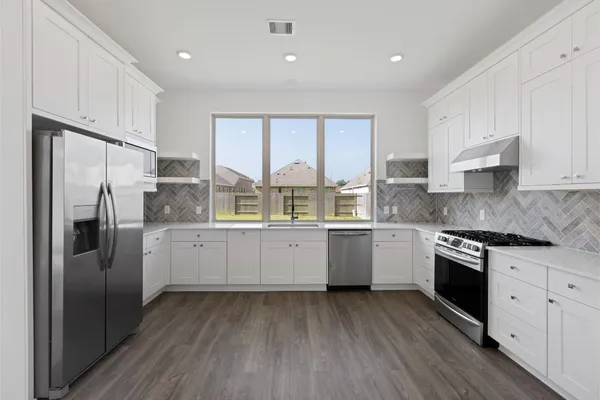 a kitchen with granite countertop a refrigerator oven a sink dishwasher and white cabinets with wooden floor