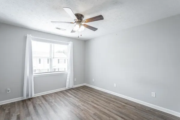 an empty room with wooden floor fan and windows
