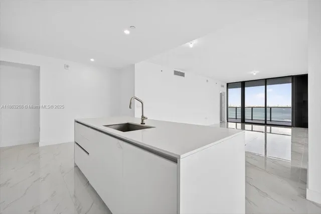 a large white kitchen with kitchen island a large window appliances and cabinets