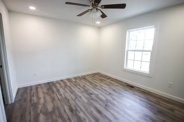 an empty room with wooden floor windows and fan