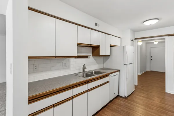 a kitchen with stainless steel appliances a sink dishwasher a refrigerator and white cabinets with wooden floor