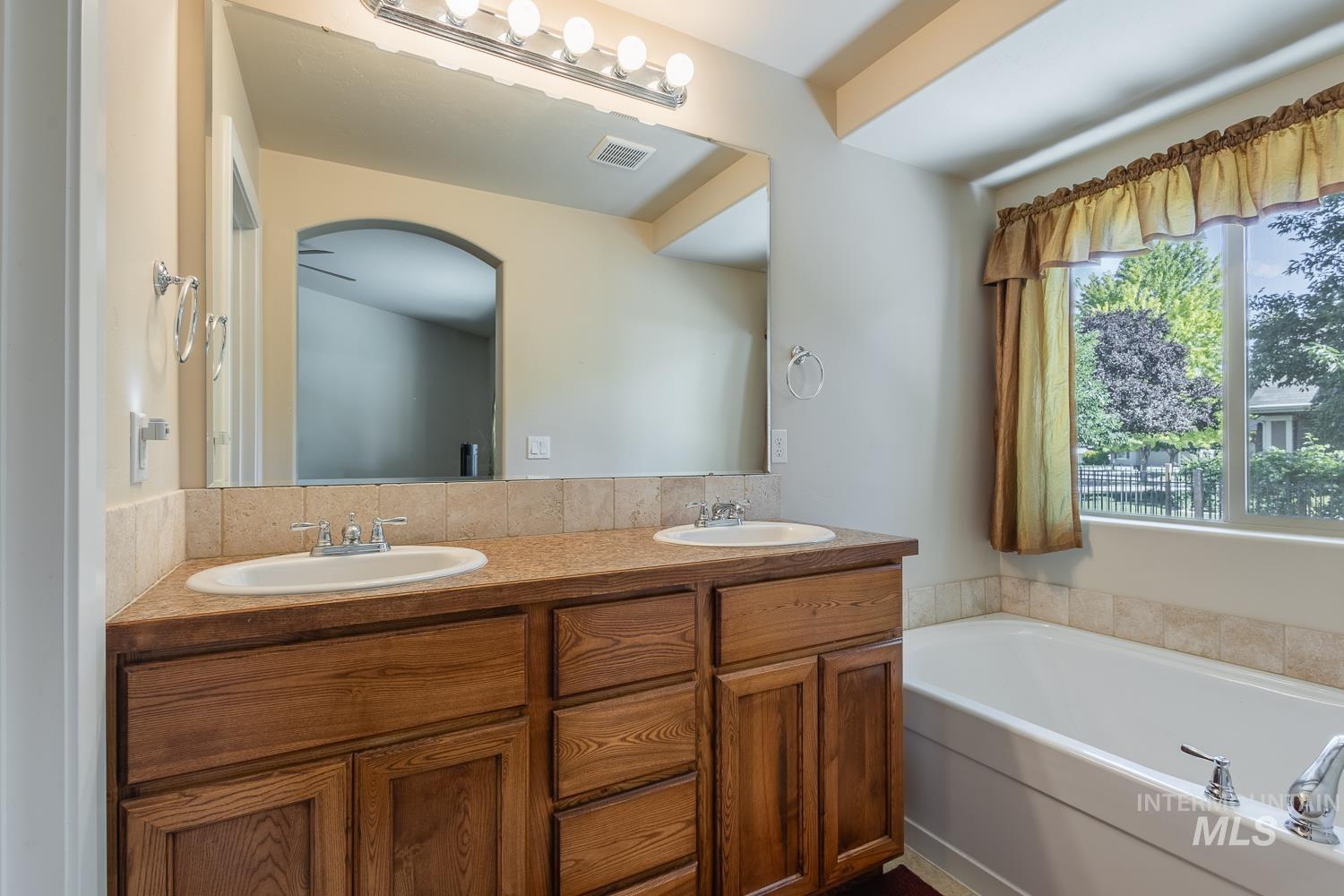 1186 East Observation Street Meridian, ID 83642 - Photo 23 of 33 Bathroom featuring a dual vanity with wood cabinetry, a large mirror, and a bathtub with a window
