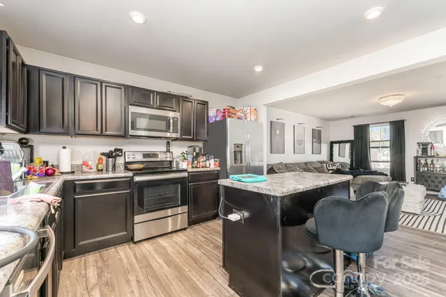 a kitchen with stainless steel appliances granite countertop a stove top oven a sink dishwasher a dining table and chairs with wooden floor