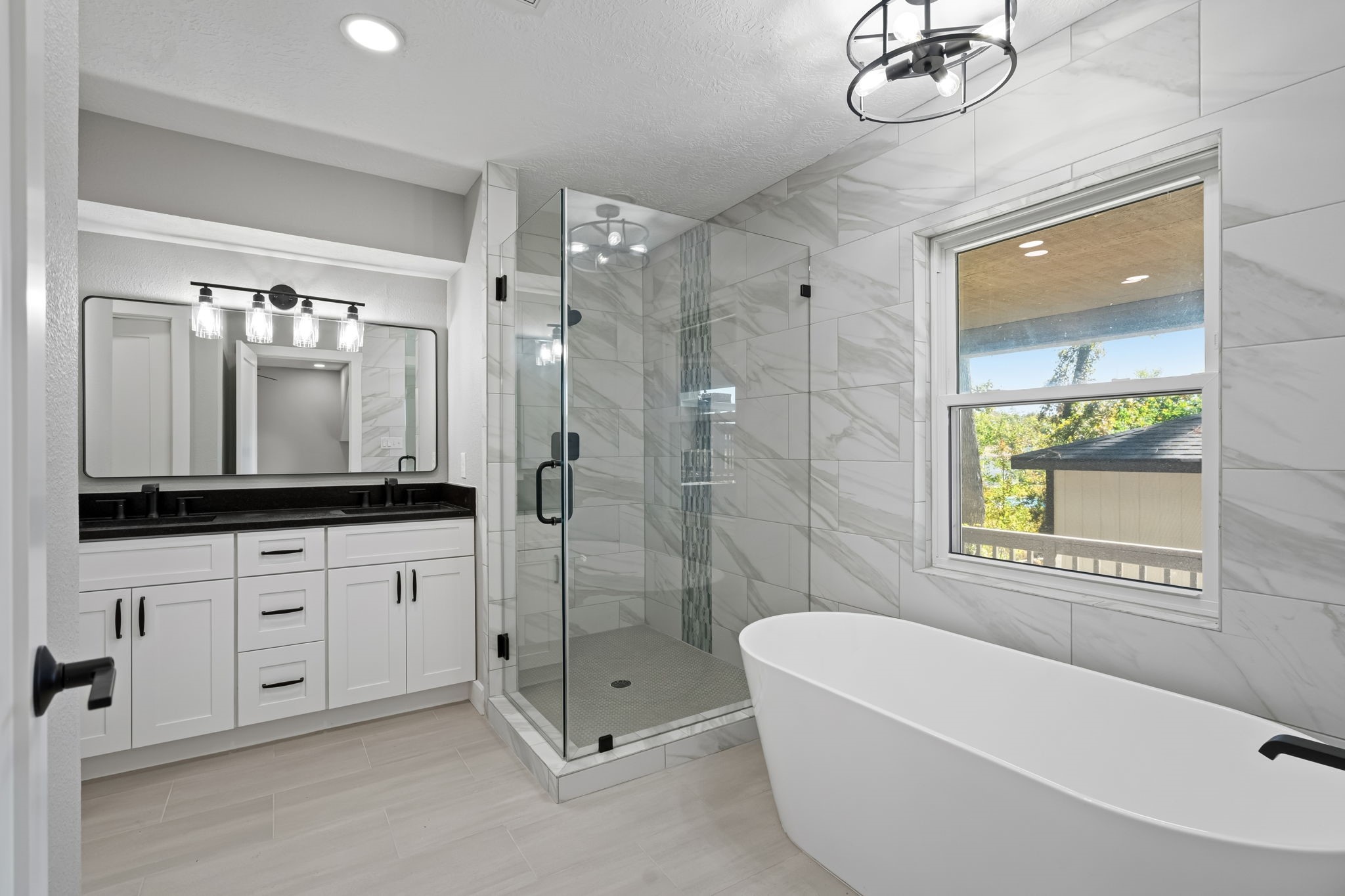 284 Hackberry Street Trinity, TX 75862 - Photo 15 of 42 The primary suite is impressive, complete with contemporary garden tub, walk in shower with frameless glass design, Shaker-style cabinetry, leathered granite countertops, undermount sinks, framed mirror, tiled accent wall, and black fixtures.