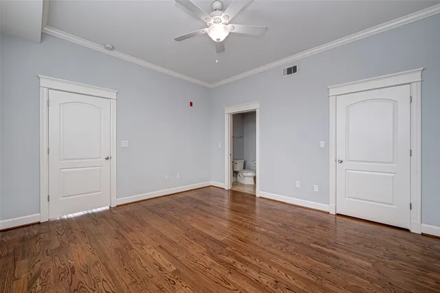 a view of an empty room with wooden floor and a ceiling fan