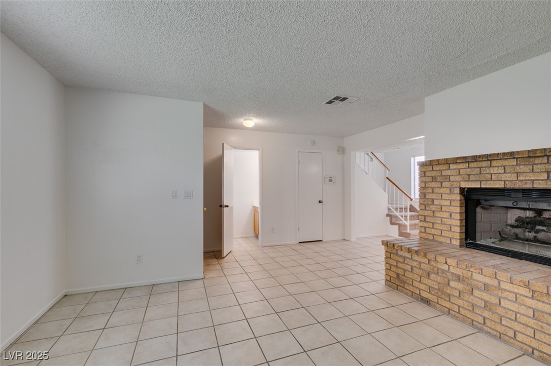 2681 Ruthe Duarte Avenue Las Vegas, NV 89121 - Photo 10 of 43 Unfurnished living room with baseboards, a textured ceiling, stairs, visible vents, and a brick fireplace