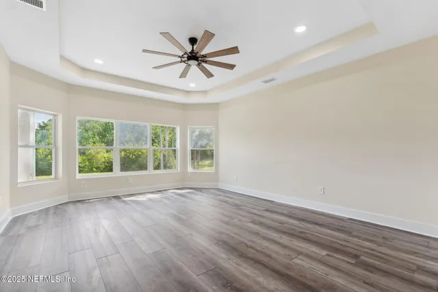 an empty room with wooden floor fan and windows
