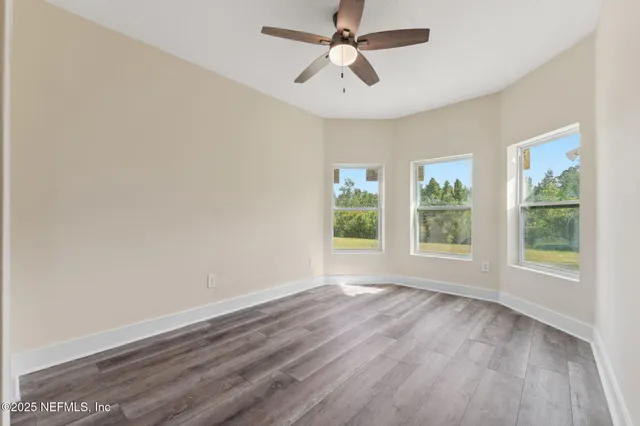 an empty room with wooden floor fan and windows