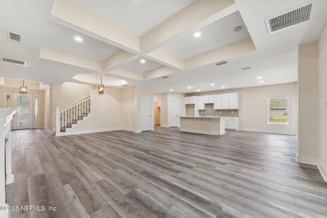 a view of an empty room and kitchen view with wooden floor