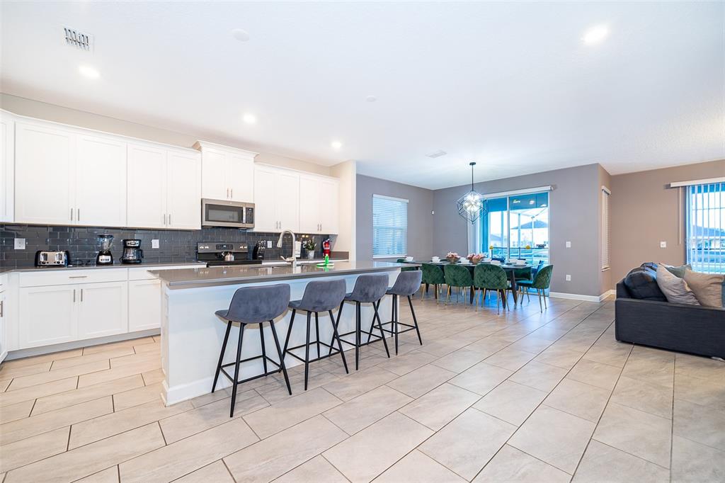 830 Sticks Street Davenport, FL 33896 - Photo 18 of 37 a kitchen with stainless steel appliances kitchen island granite countertop a refrigerator a stove a dining table and chairs with wooden floor