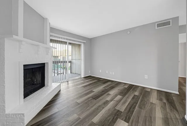 a view of an empty room with wooden floor fireplace and a window