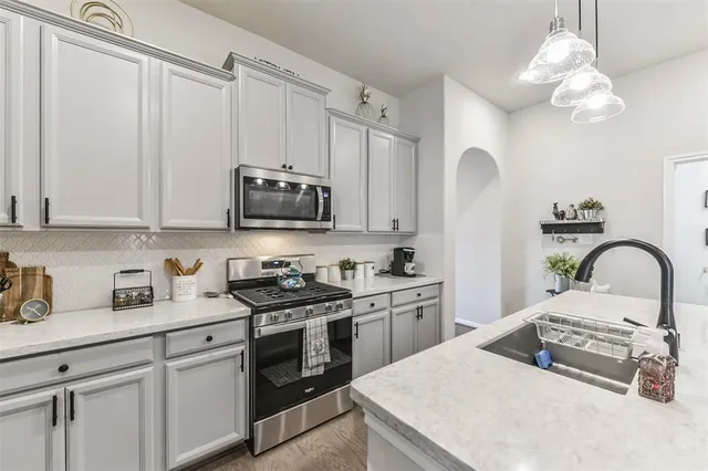 a kitchen with stainless steel appliances granite countertop a stove a sink dishwasher and white cabinets with wooden floor