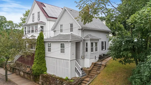 a view of a white house next to a yard with plants and trees
