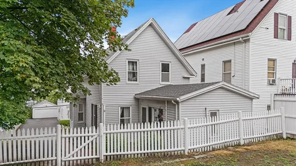 a view of a white house with a small yard and wooden fence