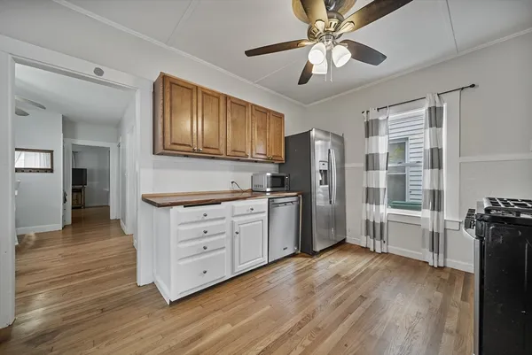 a kitchen with stainless steel appliances granite countertop a refrigerator a stove a sink and white cabinets with wooden floor next to windows