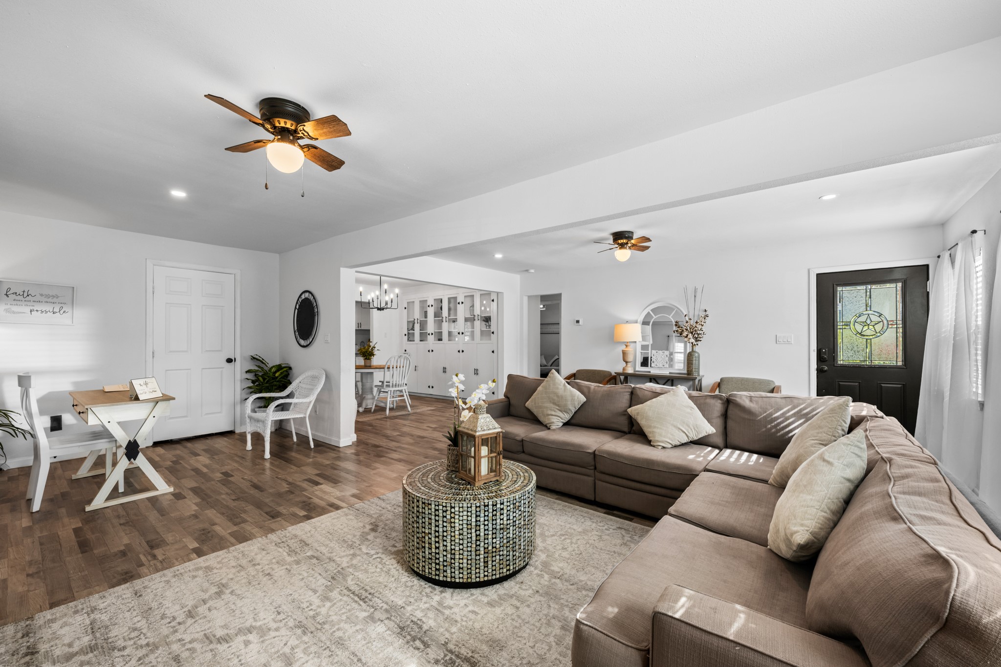 729 Kyle Angleton, TX 77515 - Photo 2 of 36 This photo showcases a spacious, open-concept living area with abundant natural light, featuring a large sectional sofa, wood-look flooring, and a cozy dining nook. The room is bright and inviting, with ceiling fans and a modern design.