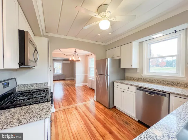 a kitchen with stainless steel appliances granite countertop a refrigerator a sink dishwasher a stove and white countertops with wooden floor