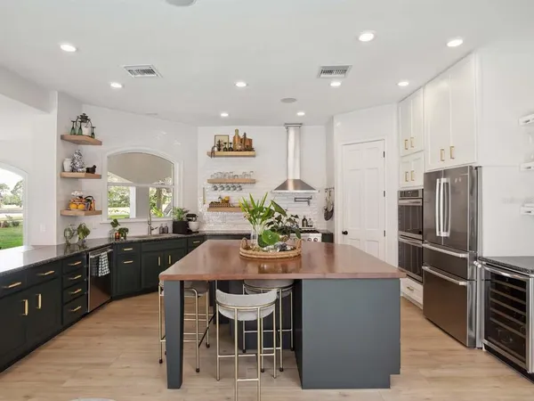 a kitchen with stainless steel appliances kitchen island granite countertop a refrigerator a stove a sink a dining table and chairs with wooden floor