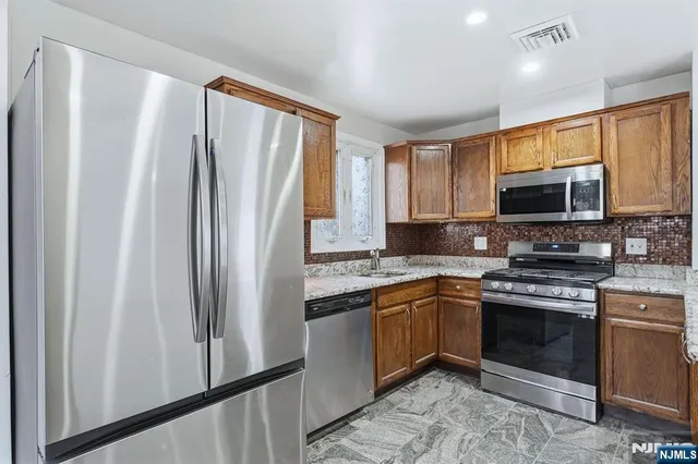 a kitchen with stainless steel appliances granite countertop a stove top oven a sink and a refrigerator with wooden floor