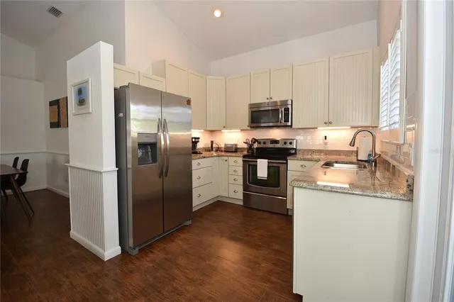 a kitchen with stainless steel appliances granite countertop a refrigerator a stove a sink a dining table and chairs