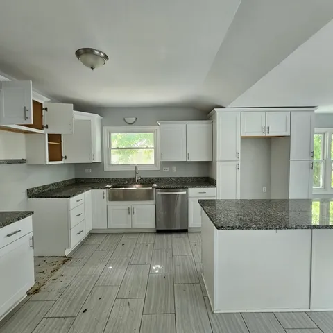 a large kitchen with granite countertop a stove top oven a sink a counter space and cabinets
