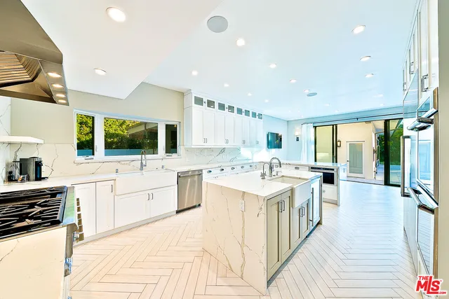a large white kitchen with a stove top oven a sink dishwasher and white cabinets with wooden floor