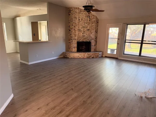 an empty room with wooden floor fireplace and windows
