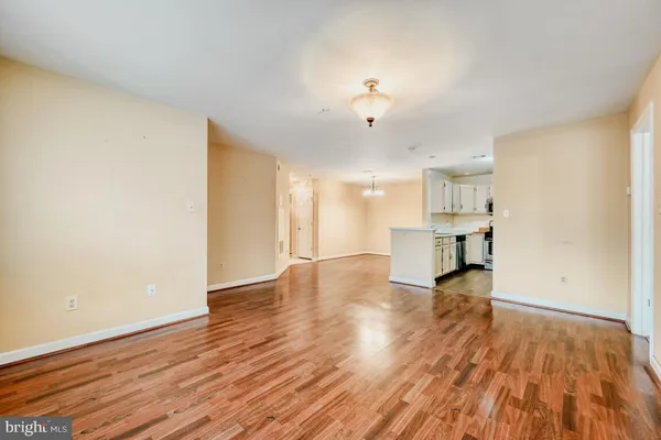 a view of empty room with wooden floor and kitchen