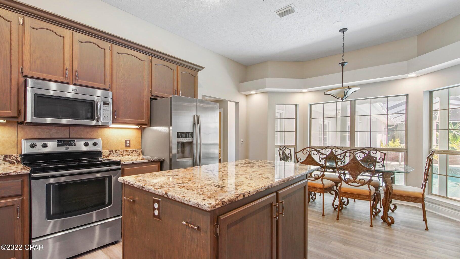 104 Colony Harbour Road Panama City Beach, FL 32407 - Photo 22 of 75 a kitchen with stainless steel appliances granite countertop a stove top oven a sink dishwasher a dining table and chairs with wooden floor