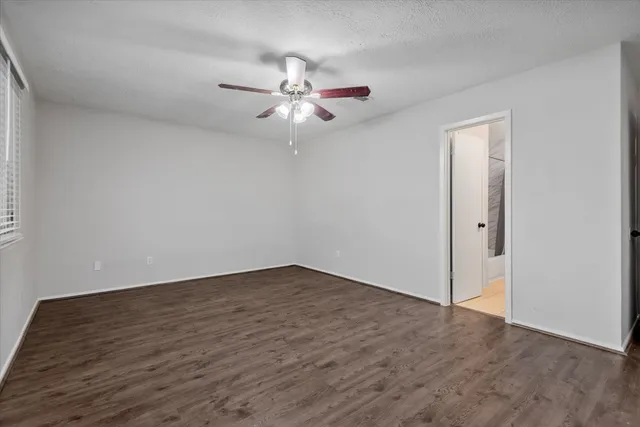 an empty room with wooden floor fan and windows