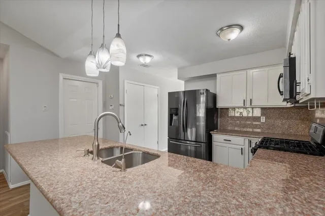 a kitchen with stainless steel appliances granite countertop a refrigerator a sink a stove a dining table and chairs