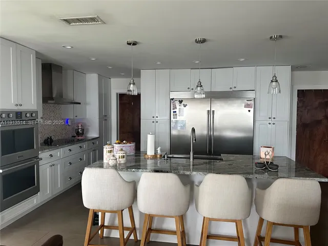 a kitchen with stainless steel appliances a dining table chairs refrigerator and sink