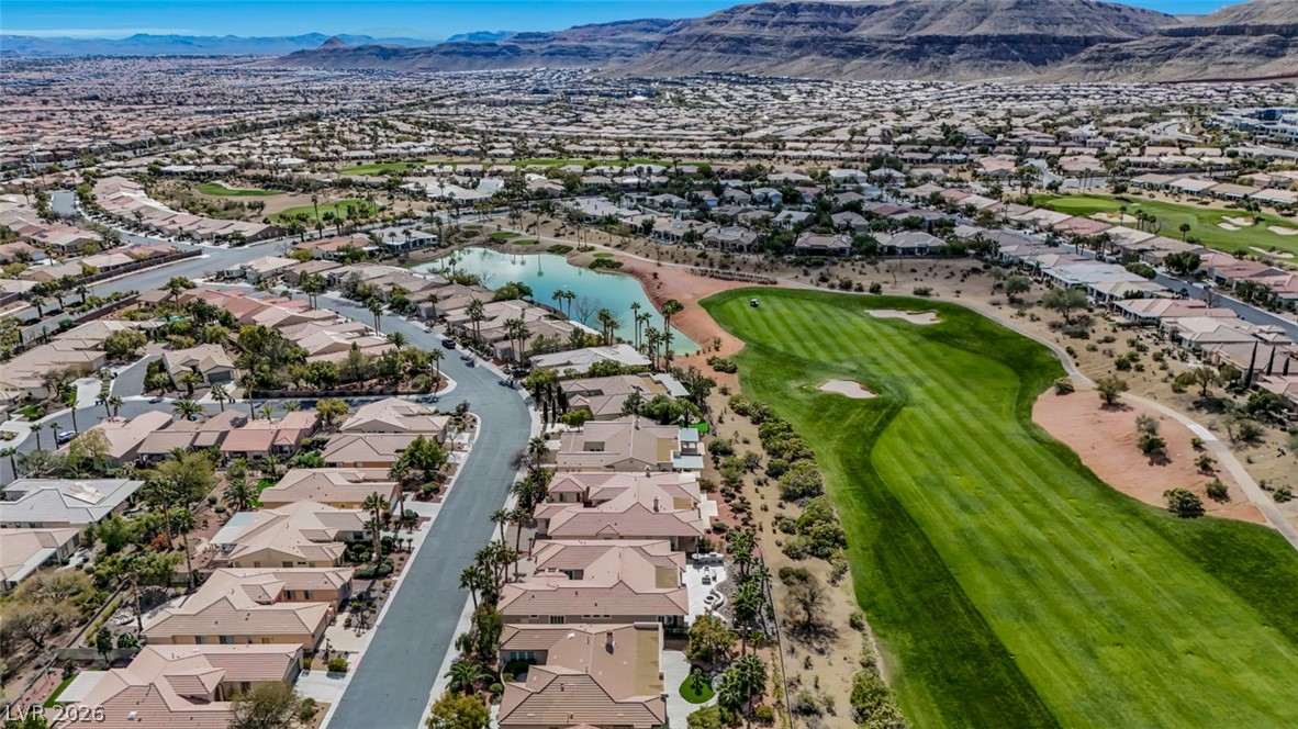 5015 Rivedro Street Las Vegas, NV 89135 - Photo 73 of 91 An aerial perspective reveals a serene golf course community, featuring a pristine green, tranquil pond, and surrounding residences under a vast sky.