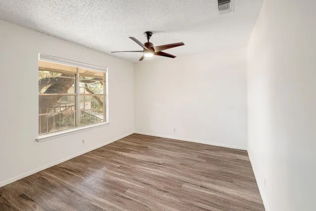 an empty room with wooden floor ceiling fan and windows