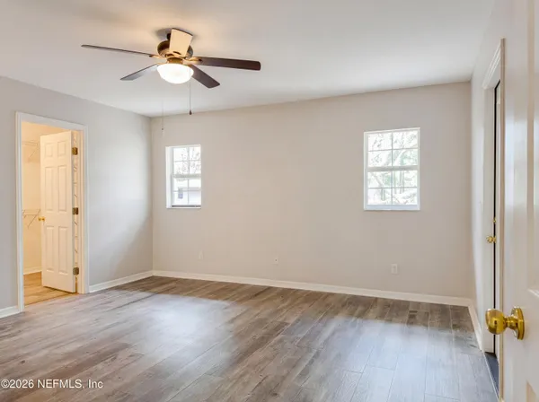 an empty room with wooden floor chandelier fan and windows