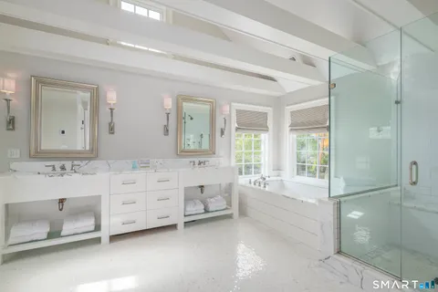 a spacious bathroom with double vanity a sink a mirror a bathtub and next to a window