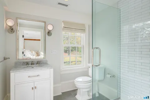 a bathroom with a granite countertop toilet a sink a mirror and a window