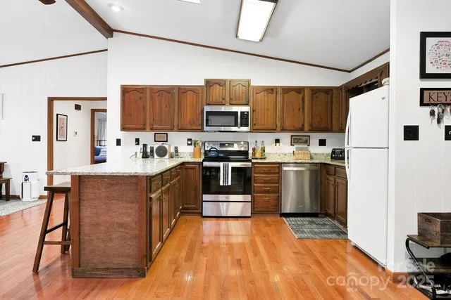 a kitchen with stainless steel appliances granite countertop a stove top oven a sink dishwasher and a refrigerator with wooden floor