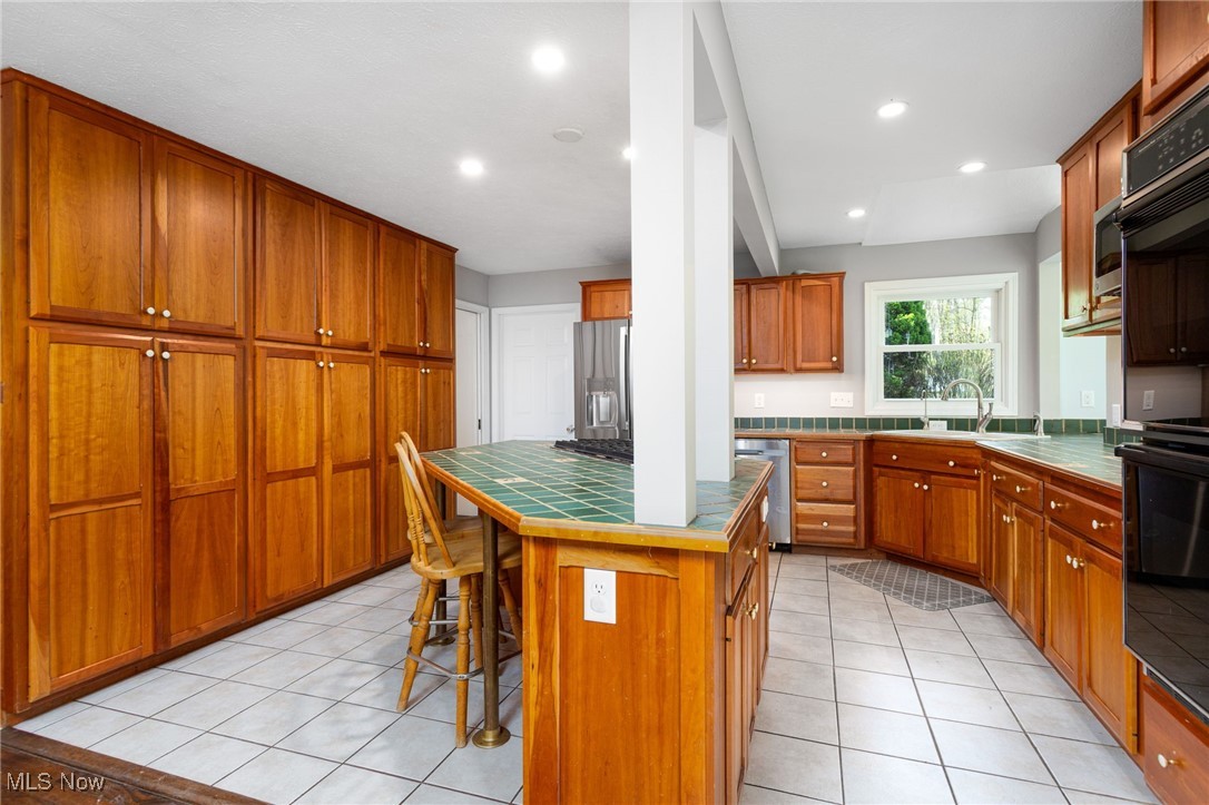 14566 West Ridge Road Novelty, OH 44072 - Photo 22 of 49 Kitchen featuring light tile patterned floors, tile countertops, a sink, and a kitchen bar