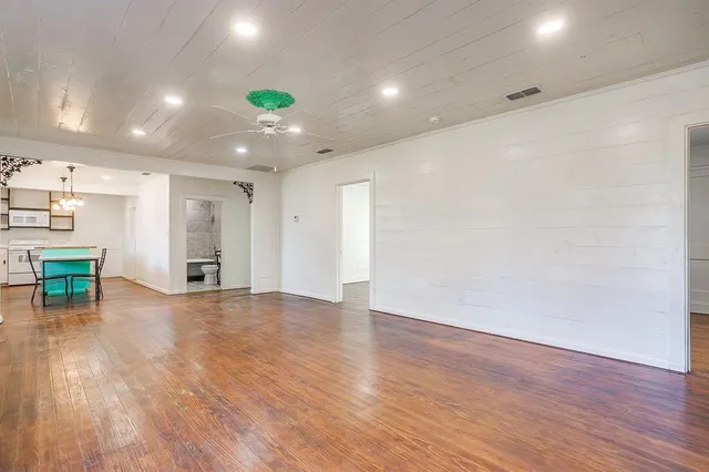 a view of an empty room with wooden floor and a kitchen