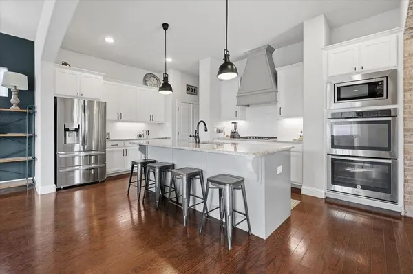 a kitchen with stainless steel appliances granite countertop a refrigerator a stove a microwave and a wooden floor