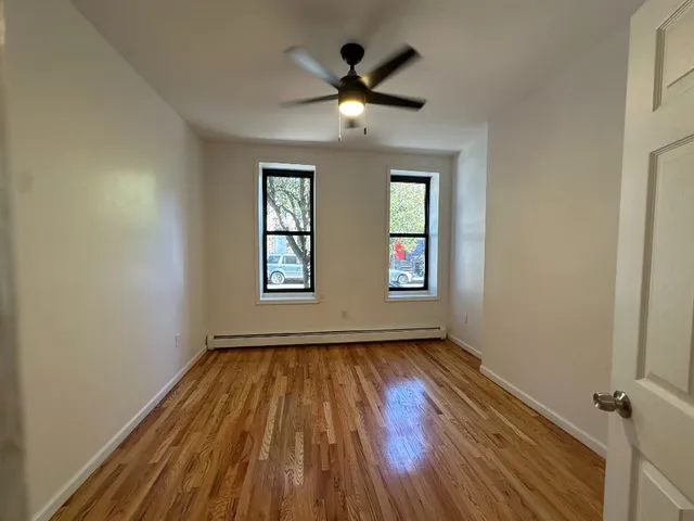 an empty room with wooden floor chandelier fan and windows