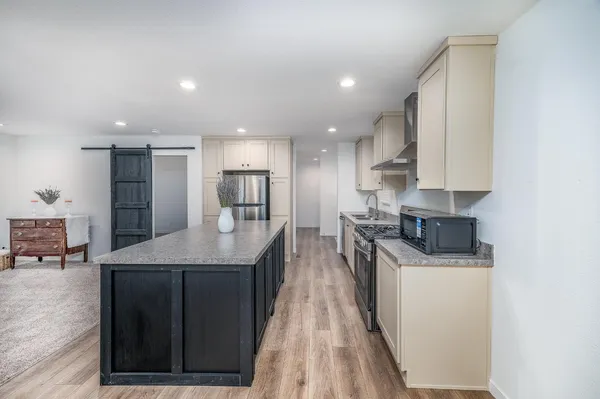 a kitchen with stainless steel appliances granite countertop a stove a sink a refrigerator and white cabinets with wooden floors